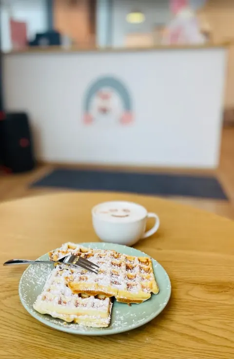 Frische Waffeln mit Puderzucker und ein Cappuccino auf einem Tisch im Happy Kids Café